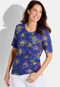 Bluse mit kurzen Ärmeln in Blau mit rundem Halsausschnitt. Sie hat ein lebhaftes Blumenmuster in Gelb, Pink und Blau auf einem dunklen Hintergrund.