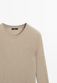 Beige geribbelde lange mouwen top met een ronde halslijn. Heeft een subtiele textuur en een label bij de kraag. Gemaakt van zacht, rekbaar materiaal.