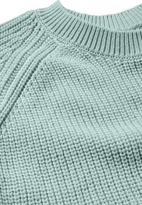 Pull en maille vert clair avec un col côtelé, un motif texturé et une coupe décontractée avec des détails de couture visibles.