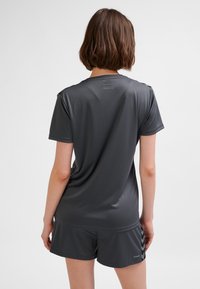 Grå träningsskjorta med korta ärmar, tillverkad av ett mjukt tyg. Har en diskret logga på övre delen av ryggen och matchande shorts.