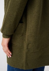 Gebreide cardigan in olijfgroen, met een ribbelzoom en -mouwen. Inclusief zijzakken, laat een zachte textuur en een casual pasvorm zien.