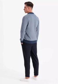 Sudadera para hombre en azul claro, con un tejido texturizado, cuello navy y pantalones oscuros con dobladillo. El modelo lleva zapatillas blancas.