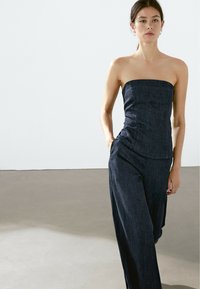 Sukně bez ramínek z temného denimu s přiléhavým trupem, širokými nohavicemi a jemnými prošívacími detaily. Hladká textura, minimalistický design.