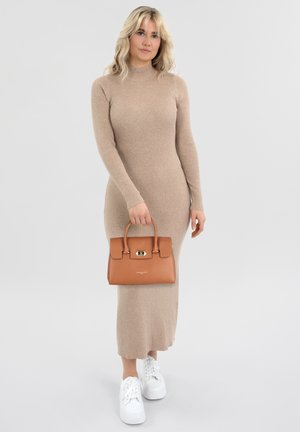 Abito lungo beige a coste, borsa rigida marrone con chiusura dorata, sneakers bianche, modella in posa contro uno sfondo neutro.