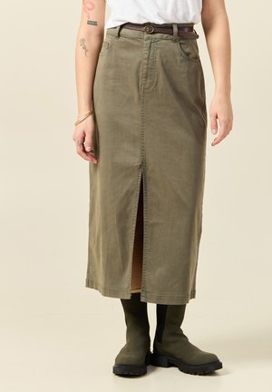 Jupe maxi olive avec une fente à l'avant, fabriquée en coton doux. Présente des passants de ceinture et deux poches latérales. Assortie à des bottes jusqu'aux genoux.