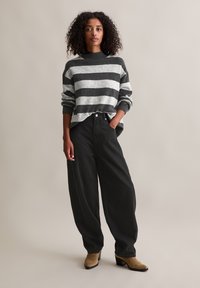 Pull rayé noir et gris avec un col montant et une coupe décontractée, associé à un pantalon noir taille haute et des bottines à talons beige.