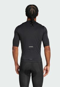 Black athletic shirt with short sleeves, featuring a slim fit and textured fabric; has a reflective accent on the back and logo detail at the hem.