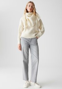 Crème wollen trui met een gestructureerd patroon en geribbelde zoom, gecombineerd met lichtgrijze rechte spijkerbroek en witte sneakers.