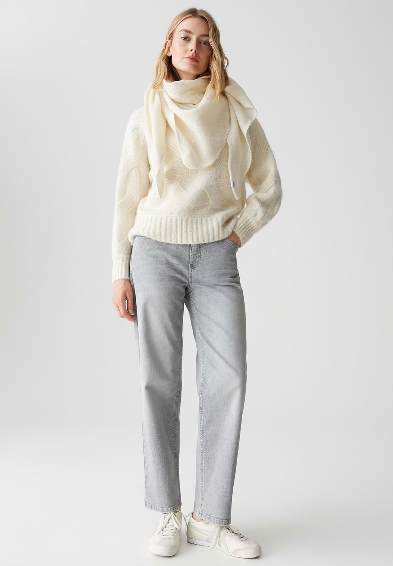 Crème wollen trui met een gestructureerd patroon en geribbelde zoom, gecombineerd met lichtgrijze rechte spijkerbroek en witte sneakers.