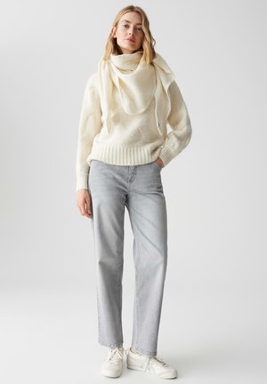 Cremfarbener Wollpullover mit strukturiertem Muster und geripptem Saum, kombiniert mit hellgrauen, geraden Jeans und weißen Sneakern.