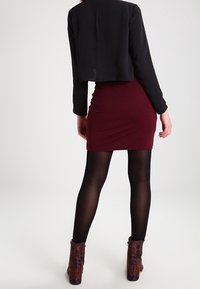 Černá zkrácená bunda, vínové bodycon šaty, průsvitné černé punčochy a vzorované kotníkové boty s detailem na zip. Pohled zezadu na outfit.