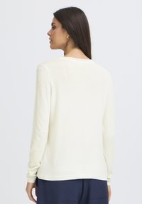 Pull à manches longues de couleur crème avec un col en dents de scie et des manches ajustées, doté d'une texture lisse et d'une coupe décontractée à l'ourlet.