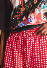 Red and white checkered pajama shorts with an elastic waistband and tie, paired with a festive graphic print top featuring candles and ornaments.