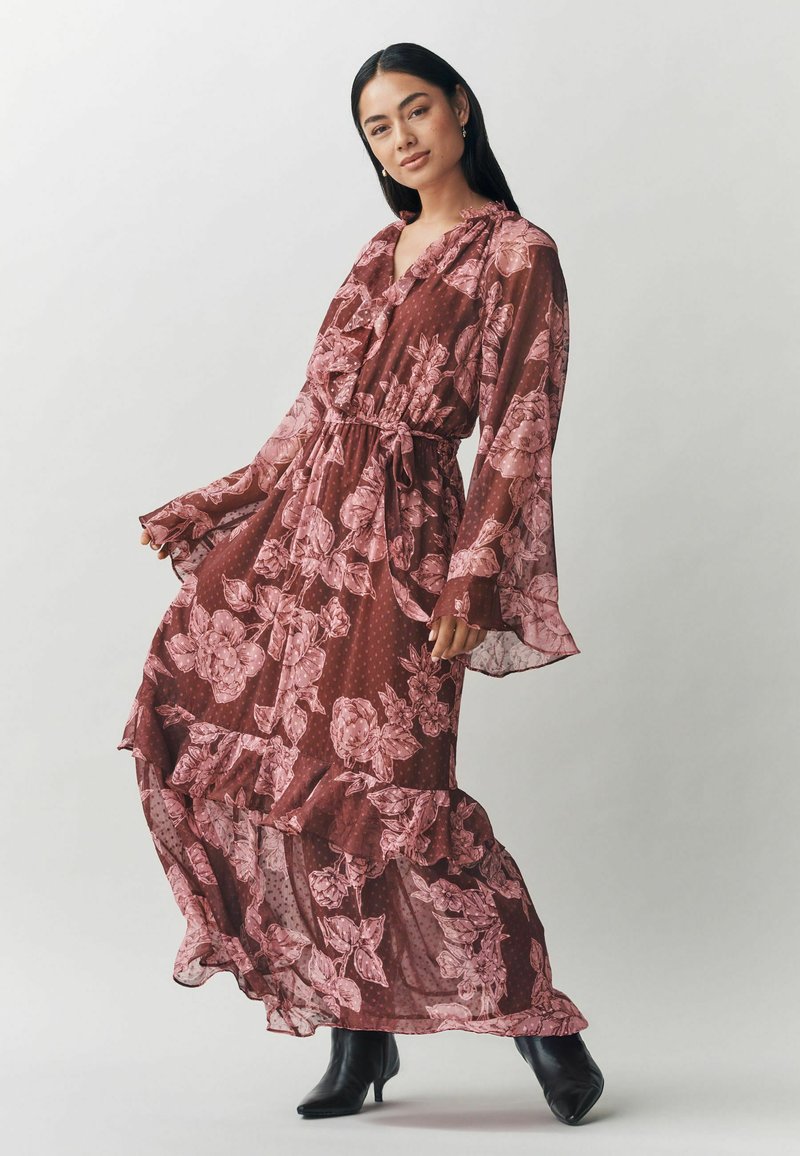 Bordo maxi suknelė su rožine gėlių raštu, raukšlėmis, ilgomis rankovėmis ir aptemptu juosmeniu. Pagaminta iš lengvos, permatomos medžiagos.