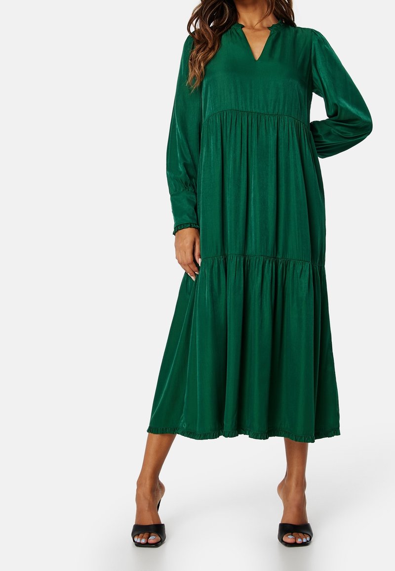 Grön maxi-klänning med V-ringning, långa ärmar, volangade lager och rynkad nederkant. Tillverkad av ett mjukt tyg, med en avslappnad passform.