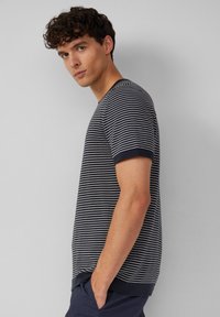 T-shirt w paski w kolorze granatowym i białym, z krótkimi rękawami i okrągłym dekoltem; materiał wydaje się miękki i lekki, z jednolitym granatowym wykończeniem przy rękawach i u dołu.