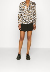 Blusa a maniche lunghe con motivo leopardato in beige, marrone e nero; presenta un scollo a V e polsini elastici, abbinata a una gonna nera.