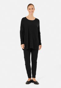Losse zwart lange mouwen top gecombineerd met zwarte smalle broek. Glad materiaal, relaxte stijl, ronde halslijn en platte schoenen.