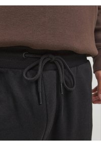 Černé tepláky s šňůrkou v pase, vyrobené z texturované látky a s jemnými žebrovanými detaily na pásku. Jednobarevné tmavé provedení.