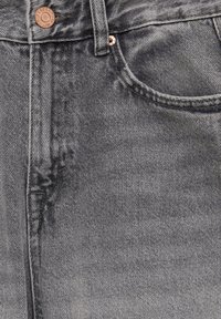 Jeans de mezclilla gris oscuro con una textura suave, que presentan un botón de cobre y un discreto detalle de costura a lo largo de la cintura y los bolsillos.