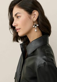 Black leather jacket with a large collar, paired with gold and pearl bee-shaped earrings, featuring intricate detailing and mixed textures.