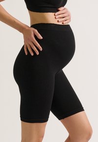 Zwarte geribbelde leggings met een middelhoge taille. Zachte textuur, knie-lengte. Ontworpen voor comfort en ondersteuning tijdens de zwangerschap. Geen zichtbare patronen.