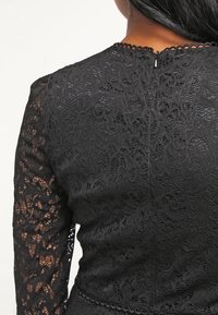 Svart spetsklänning med långa ärmar, med intrikata blommönster. Vågig halsringning och dragkedjedetalj på ryggen. Mjuk textur.