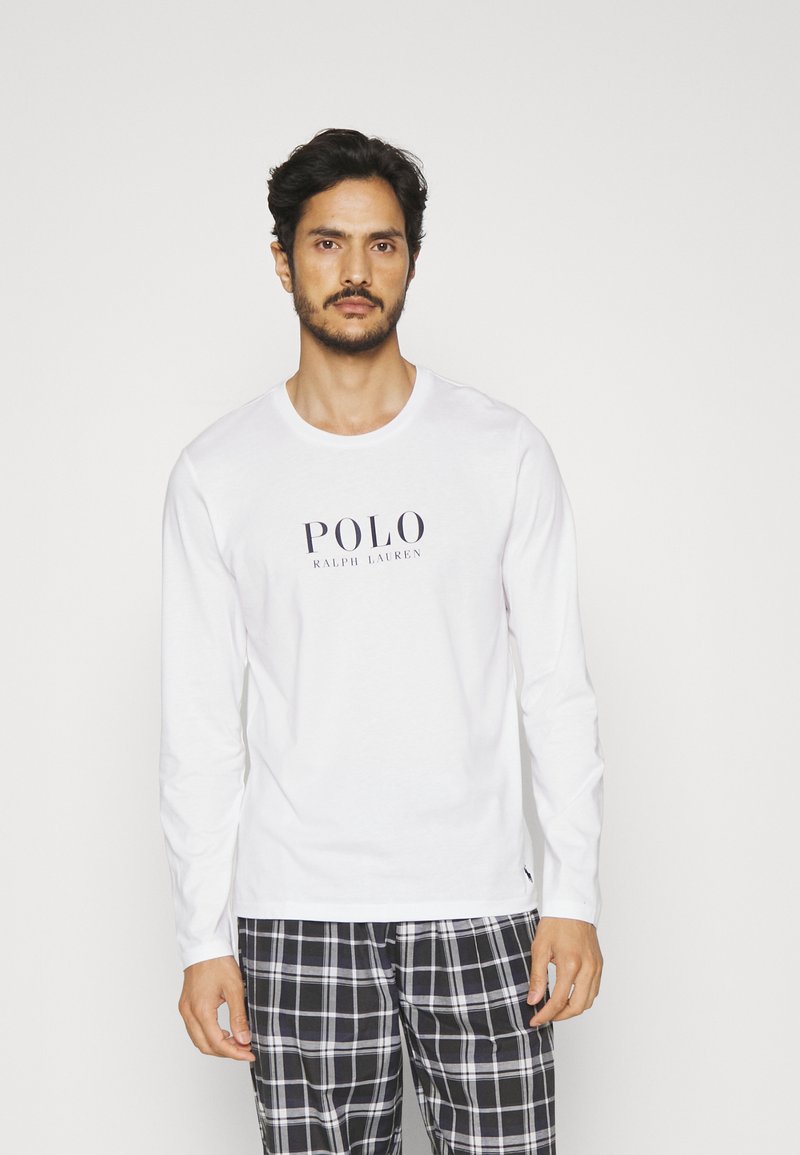 Biela košeľa s dlhým rukávom s námořníckym logom "POLO RALPH LAUREN", v kombinácii s čierno-bielymi kockovanými pyžamovými nohavicami. Tkanina vyzerá hladko.