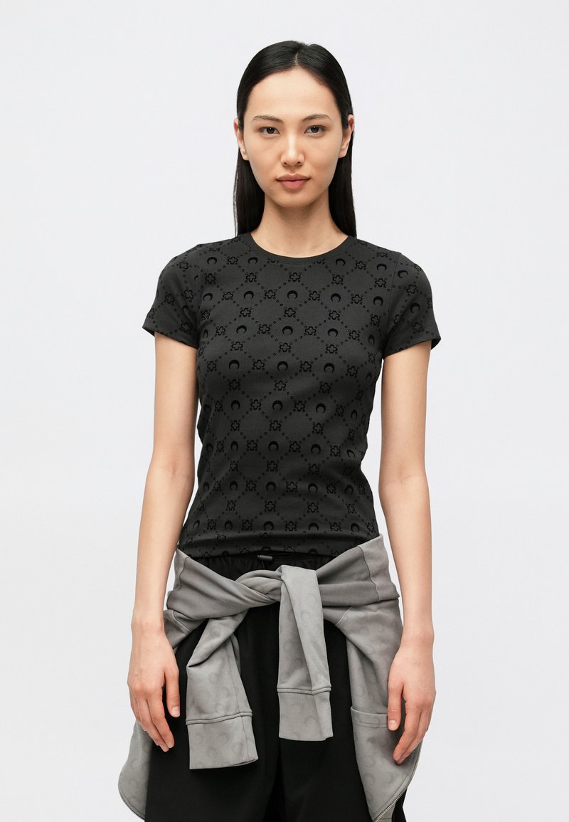 T-shirt preta de manga curta com padrão texturizado, decote redondo e corte ajustado. Uma sweatshirt cinza está amarrada à cintura.