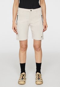 Beiga shorts med en slät textur, bältesömmar och två zipparade sidofickor. Har en logotyp på nedre benet, i kombination med beiga skor och svarta strumpor.