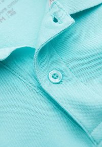 Tyrkysová polo košile s texturovanou tkaninou, která má tři knoflíky a jeden knoflík viditelný na límci.
