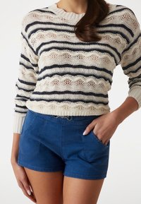 Pletený svetr s námořnickými pruhy a otevřeným vzorem, kombinovaný s modrými džínovými šortkami s předními kapsami a přiléhavým pasem.