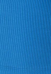 Gros plan d'un tissu côtelé bleu avec des coutures verticales visibles et des détails de texture.