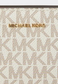 Michael Kors bézs színű pénztárca texturált anyagból, finom MK mintával és arany színű logóval az elején. Sima felület részletek.