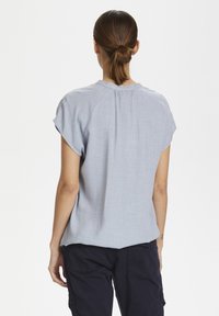 Ljusblå kortärmad skjorta med avslappnad passform, raglanärmar och en subtil textur. Har rund halsringning och detaljer med veck i ryggen.