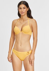 Gelbes Bikini-Set mit einem gepolsterten, dreieckigen Oberteil mit dünnen Trägern und einem tief sitzenden Unterteil, das an der Seite durch ein kreisförmiges Detail akzentuiert wird.