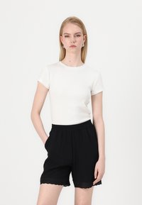 White knit short-sleeve top paired with black elastic waist shorts; shorts have textured scalloped hem detail.