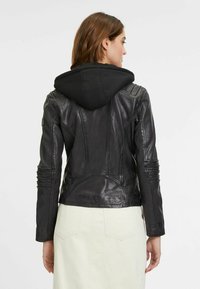 Schwarze Lederjacke mit angenähter schwarzer Kapuzenjacke, mit gerippten Schultern und eng anliegenden Ärmeln. Rückansicht zeigt eine taillierte Silhouette.