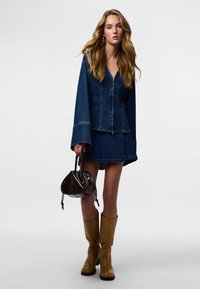 Jeans jakna z razkošnimi rokavi in izrezom v obliki črke V, kombinirana s usklajeno jeans krilo. Rjavi škornji do kolen in majhna temna torbica dopolnjujejo videz.