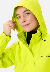 Veste imperméable jaune vif avec capuche, poignets réglables et fermeture éclair à l'avant. Logo de la marque visible sur le côté gauche.