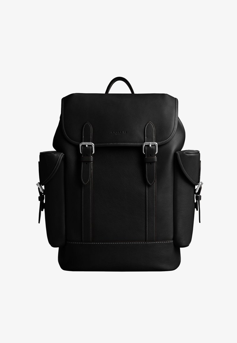 Rucsac negru din piele cu clapetă superioară, două curele cu catarame argintii, buzunare laterale cu închidere cu clapetă și o mâner superior.