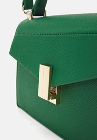 Zielona torebka skórzana o fakturze, w strukturalnym kształcie, z złotym zapięciem i wyraźnym detalem kontrastowych szwów na klapie.