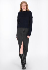 Tengerészkék kötött pulóver vállra hummal, amelyet egy elöl hasított fekete farmernadrággal párosítanak. A modellen fekete, térd fölé érő csizma van.