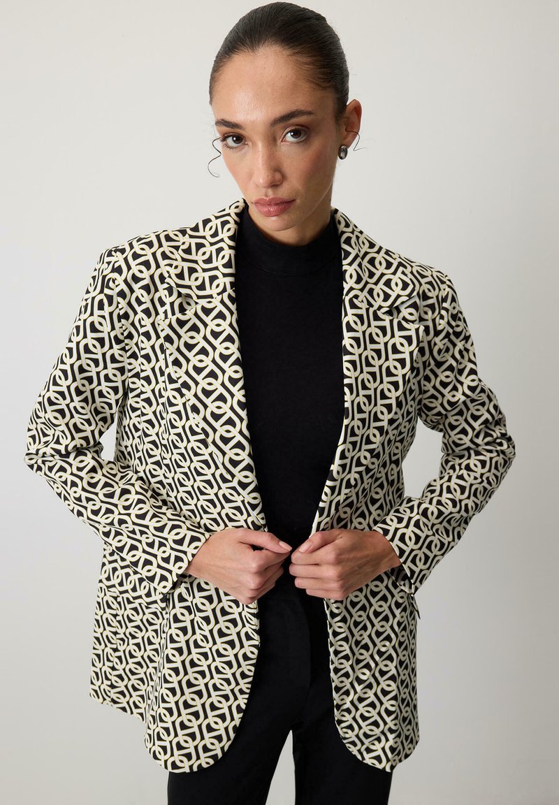 Blazer într-un model geometric crem și negru, cu rever tăiat, mâneci lungi și o croială ajustată, având un material negru contrastant dedesubt.