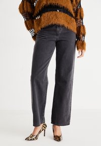 Personne portant un jean noir droit, un pull rayé brun et noir duveteux, et des chaussures à talons imprimé léopard.