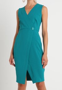 Tyrkysové bezramínkové šaty s překládaným designem, s předním rozparkem a dekorativním knoflíkovým detailem. Vyrobeno z texturované tkaniny.