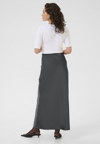 Larga y fluida falda de satén gris con una textura suave, combinada con una blusa ajustada blanca. Incluye calzado negro de tiras y cabello texturizado.