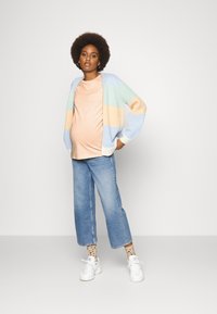Cardigan às riscas em tons pastel, top pêssego, jeans de pernas largas azuis, meias de bolinhas e ténis brancos. Textura tricotada com ajuste solto.