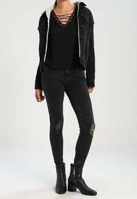 Zwarte denimjack met schapenvachtvoering, over een zwart vetertopje gedragen. Gecombineerd met zwart gescheurde skinny jeans en enkellange zwarte laarzen.