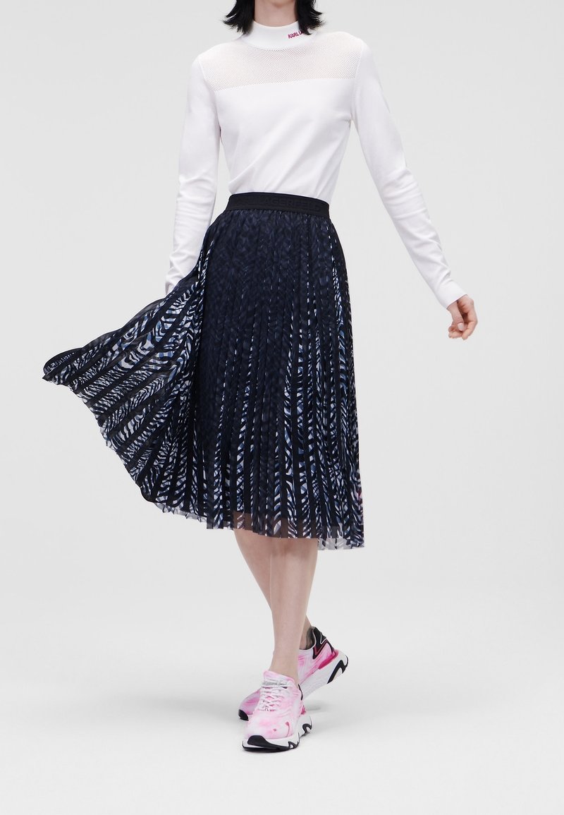Jupe plissée avec un motif abstrait bleu foncé et blanc, associée à un haut blanc ajusté. Les accessoires comprennent des baskets roses et noires.